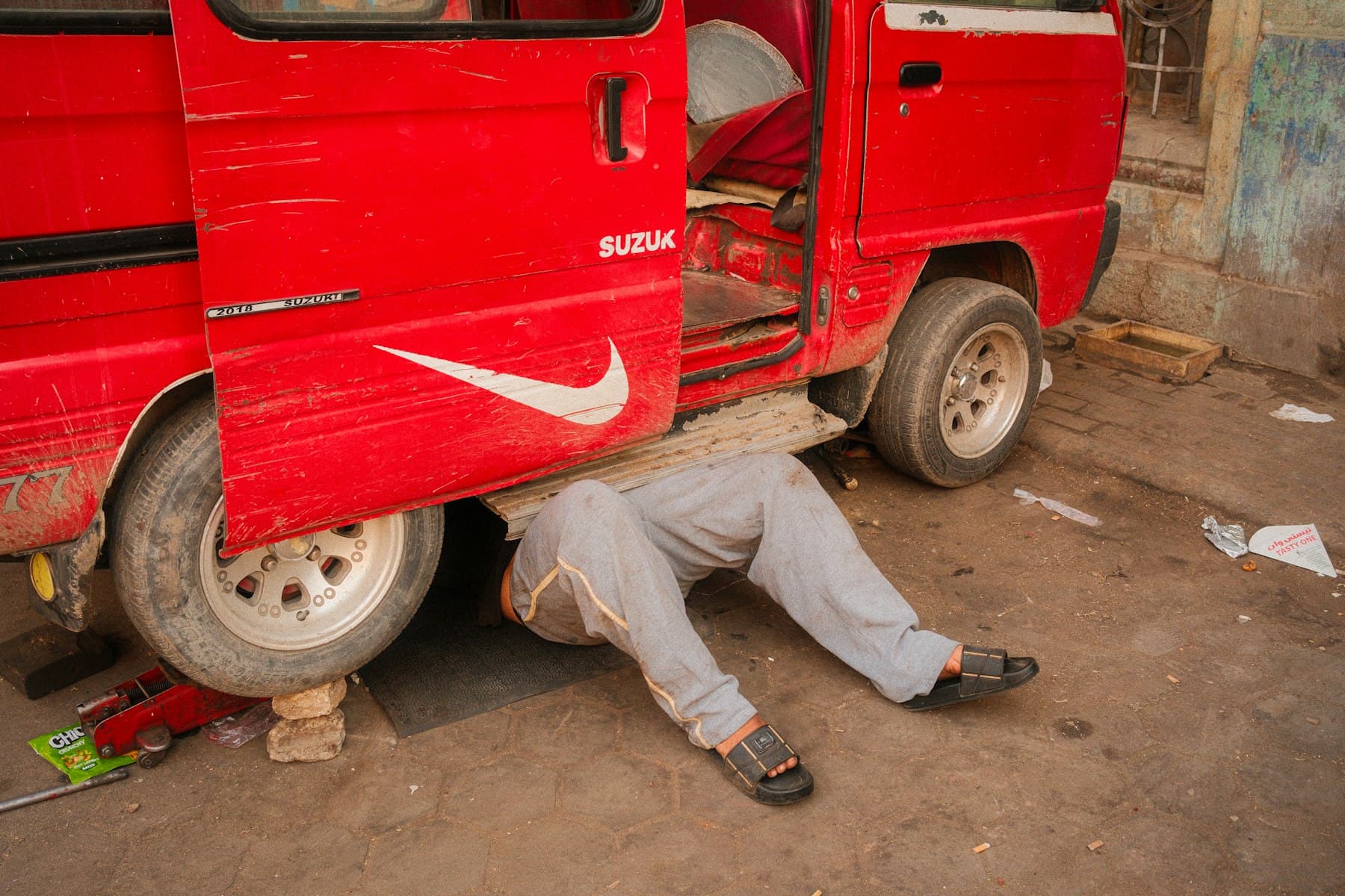 A mechanic lying under a red van, repairing it.