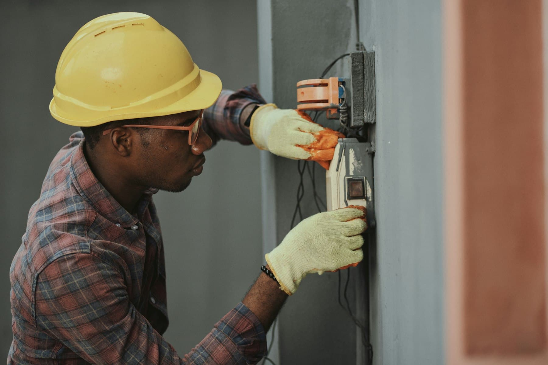 An electrician in a hard hat working on a wiring panel.